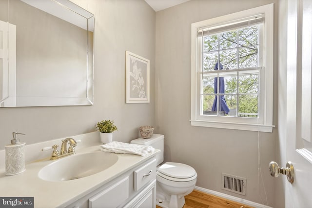 bathroom featuring toilet, baseboards, visible vents, wood finished floors, and vanity