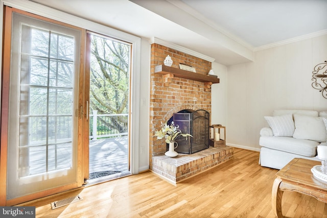 living area featuring wood finished floors, visible vents, ornamental molding, baseboards, and a brick fireplace