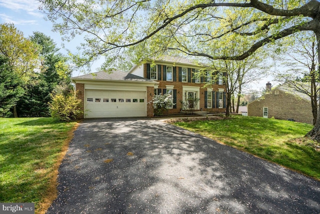 colonial house featuring brick siding, an attached garage, aphalt driveway, and a front lawn