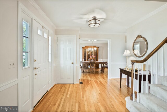 entryway featuring light wood-style flooring, crown molding, stairs, and a notable chandelier