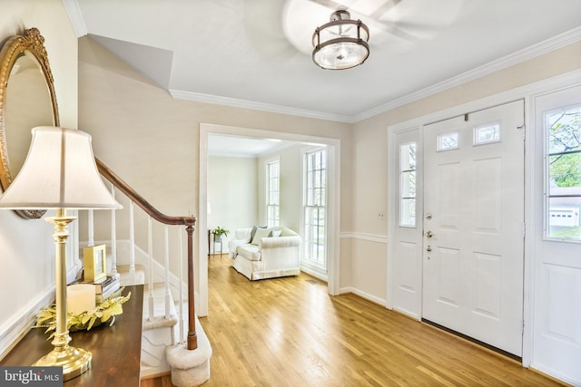 foyer featuring baseboards, wood finished floors, stairs, and ornamental molding