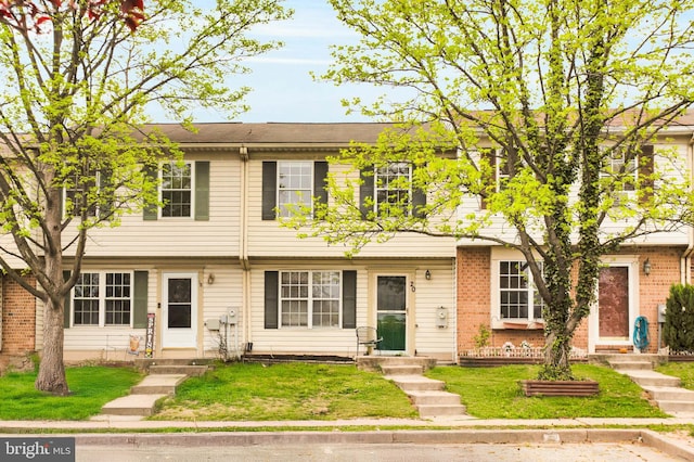 townhome / multi-family property featuring brick siding, a front yard, and entry steps