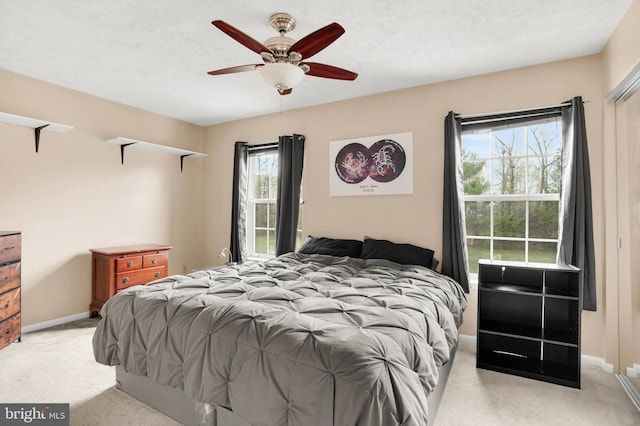 bedroom featuring a textured ceiling, baseboards, light carpet, and ceiling fan
