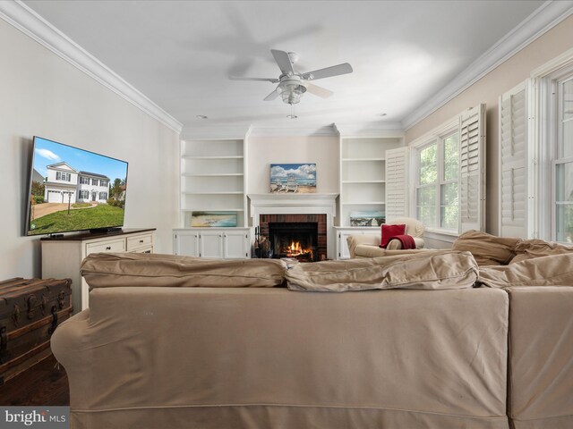 living room with built in features, ornamental molding, a fireplace, and a ceiling fan