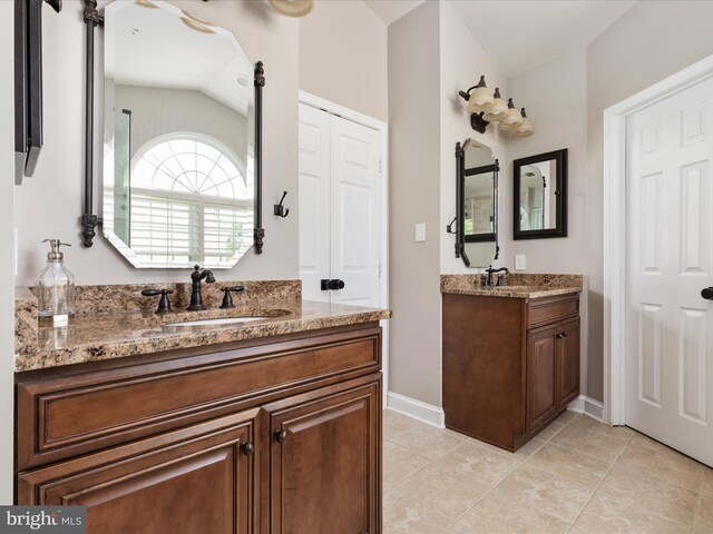 bathroom with lofted ceiling, baseboards, two vanities, tile patterned floors, and a sink