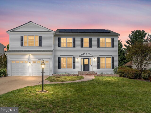 view of front of property with a garage, roof mounted solar panels, a yard, and concrete driveway