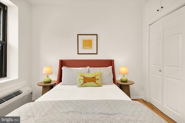 bedroom with wood finished floors, a closet, an AC wall unit, and baseboards