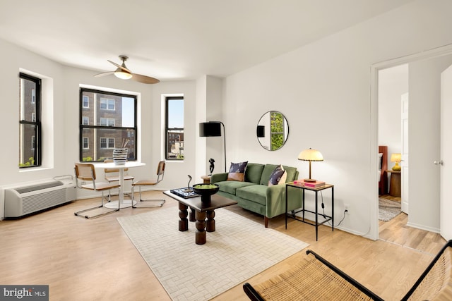 living room with a ceiling fan, wood finished floors, a wall unit AC, and baseboards