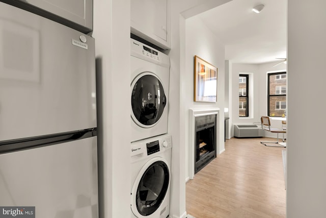 clothes washing area featuring stacked washing machine and dryer, a fireplace, light wood-type flooring, and ceiling fan