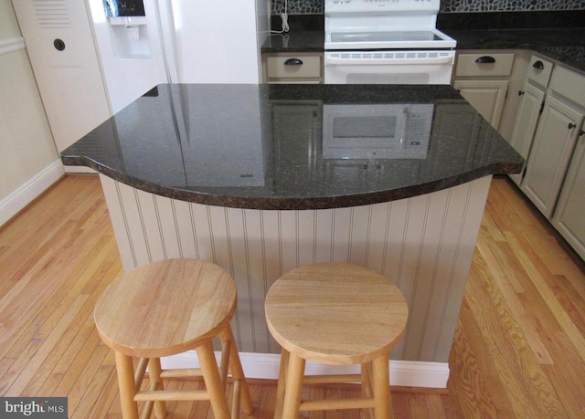 kitchen featuring dark countertops, white appliances, light wood finished floors, baseboards, and a kitchen island