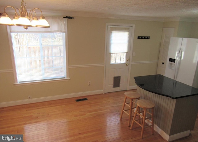 kitchen featuring dark countertops, white refrigerator with ice dispenser, light wood-type flooring, a notable chandelier, and visible vents