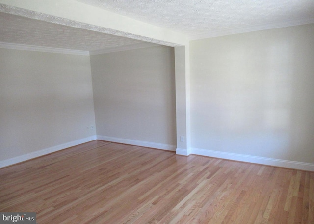 empty room featuring light wood-type flooring, a textured ceiling, crown molding, and baseboards