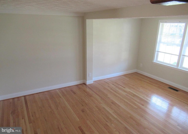 spare room with a textured ceiling, visible vents, light wood finished floors, and baseboards