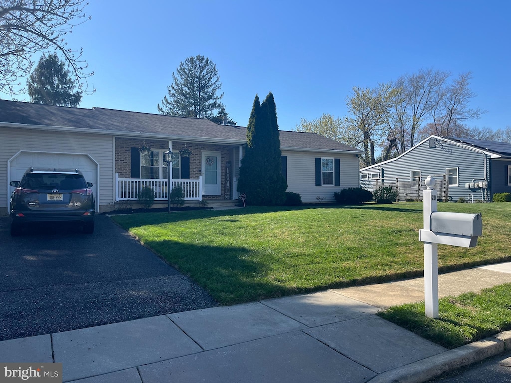ranch-style home featuring a garage, aphalt driveway, a porch, and a front lawn