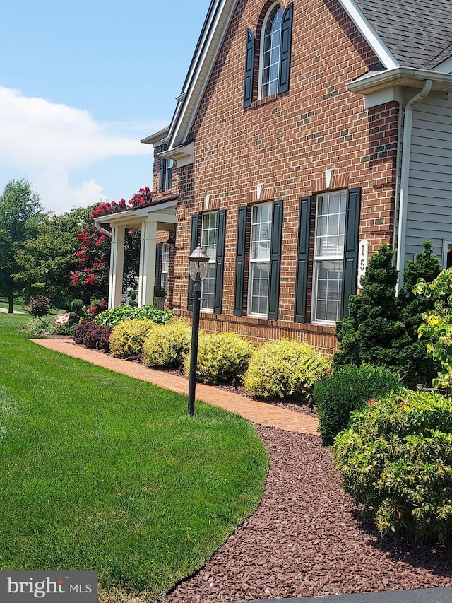 view of side of property featuring a lawn, a shingled roof, and brick siding