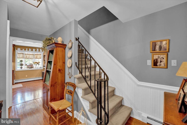 stairway featuring baseboard heating, a wainscoted wall, hardwood / wood-style flooring, and a baseboard radiator