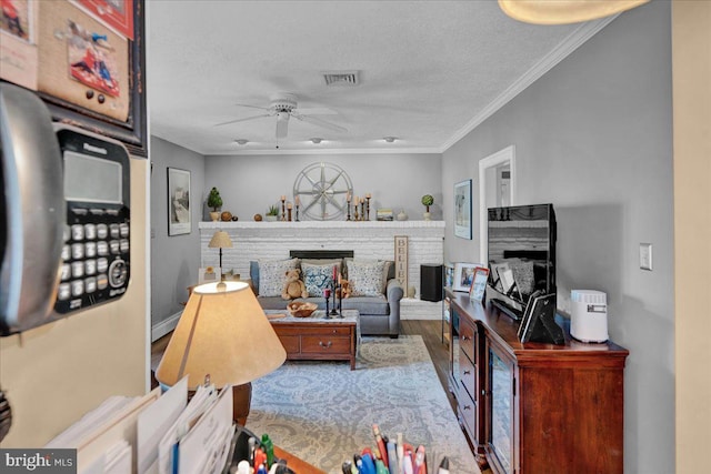 living area with a ceiling fan, wood finished floors, a textured ceiling, ornamental molding, and a fireplace
