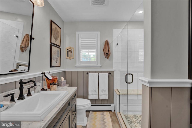bathroom featuring a baseboard radiator, a stall shower, toilet, vanity, and wainscoting