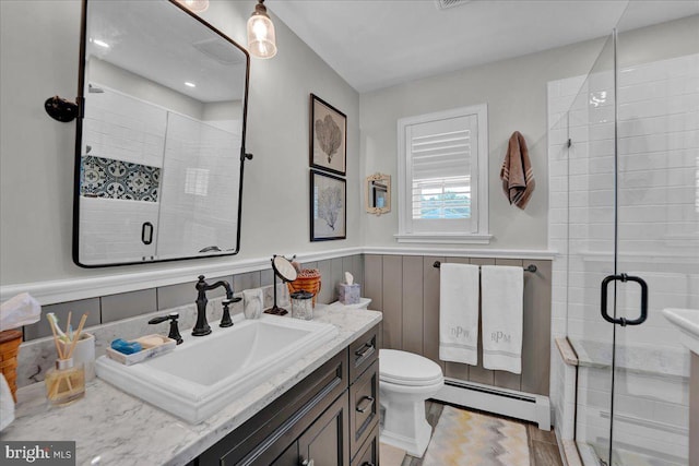 bathroom with a baseboard radiator, a stall shower, a wainscoted wall, vanity, and toilet