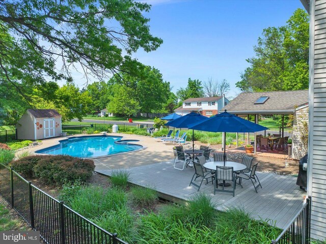 view of pool with outdoor dining area, a storage unit, fence, and a deck