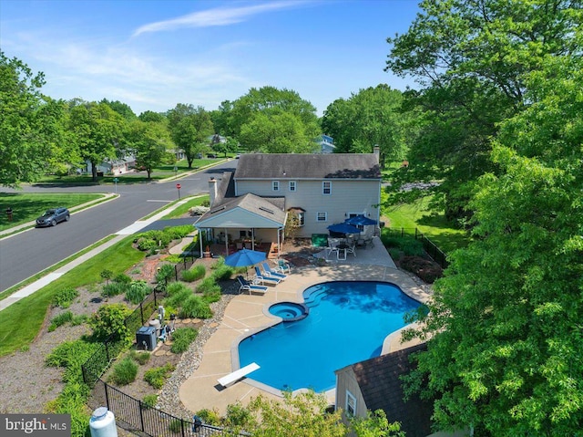 view of pool featuring fence, a patio area, a diving board, a pool with connected hot tub, and view of wooded area