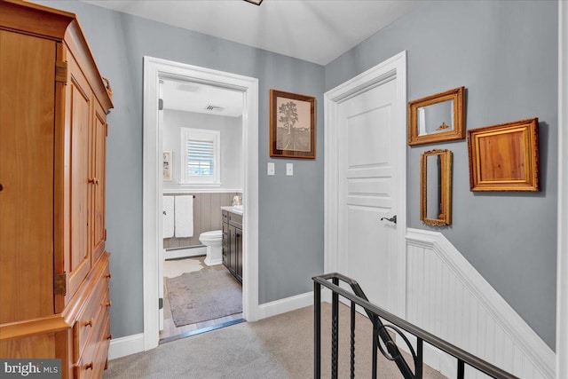 corridor featuring light colored carpet, baseboard heating, and a wainscoted wall