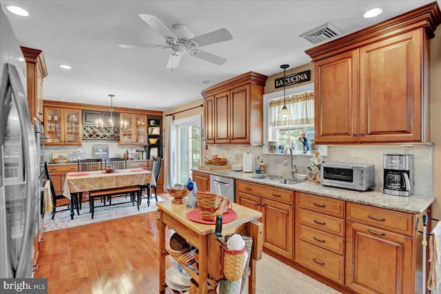 kitchen featuring a sink, stainless steel appliances, tasteful backsplash, brown cabinets, and pendant lighting