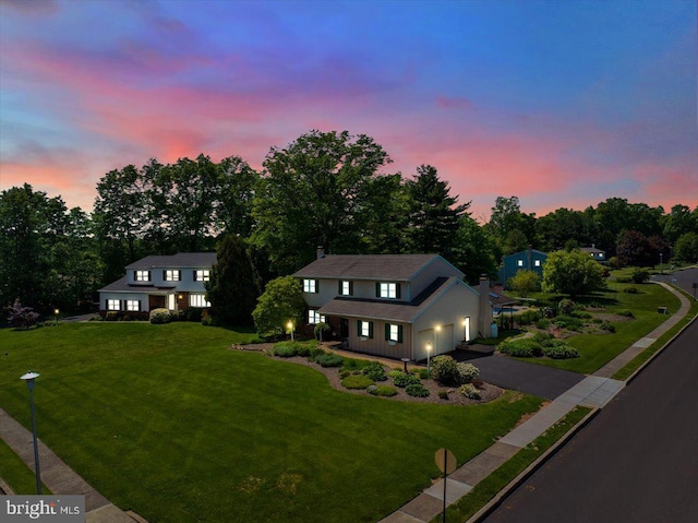 view of front of home featuring asphalt driveway, a lawn, an attached garage, and view of scattered trees