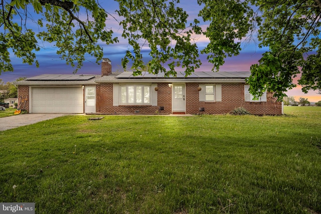 ranch-style house with a garage, solar panels, a yard, and driveway