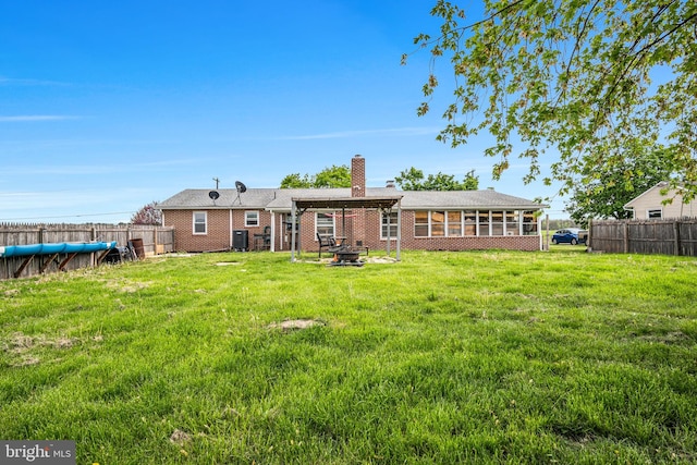 rear view of property with a fire pit, a chimney, a fenced backyard, and a sunroom