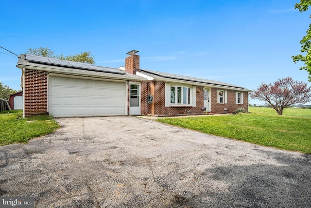 ranch-style house featuring aphalt driveway, a garage, brick siding, roof mounted solar panels, and a chimney