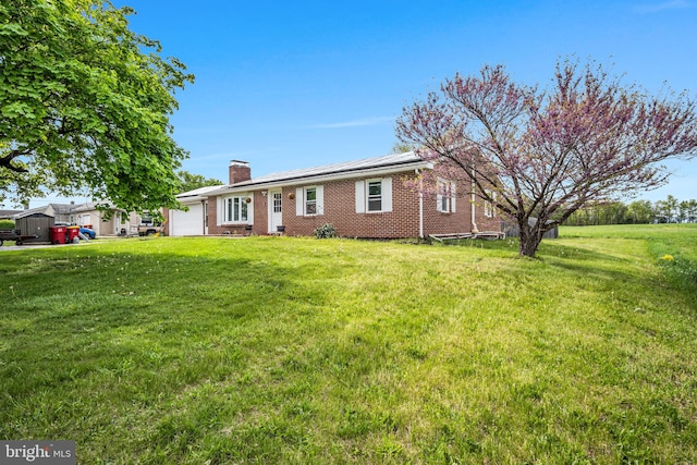 ranch-style home with a chimney, an attached garage, brick siding, and a front yard