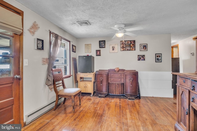 living area with ceiling fan, a textured ceiling, visible vents, wood finished floors, and a baseboard radiator