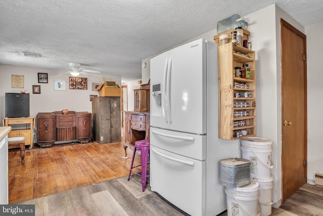 kitchen with light wood-style floors, a textured ceiling, white fridge with ice dispenser, a ceiling fan, and visible vents