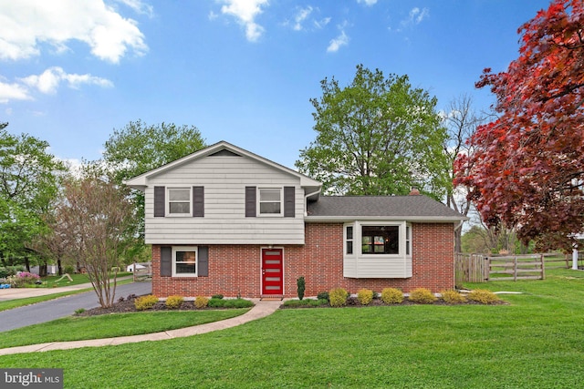 tri-level home featuring a front yard, fence, a chimney, and brick siding