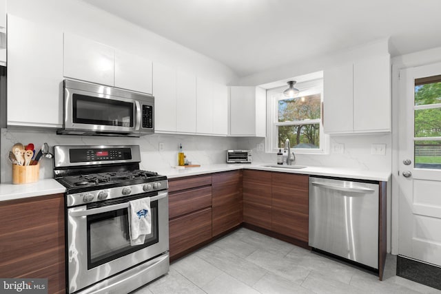 kitchen with modern cabinets, a sink, light countertops, white cabinets, and appliances with stainless steel finishes