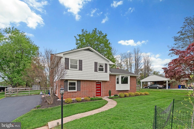 tri-level home with driveway, a carport, a front yard, fence, and brick siding