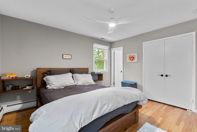 bedroom with a ceiling fan, wood finished floors, a baseboard heating unit, and a closet