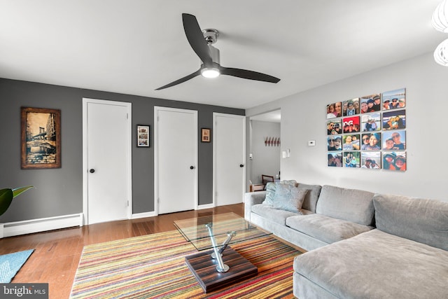 living room featuring baseboard heating, baseboards, wood finished floors, and a ceiling fan