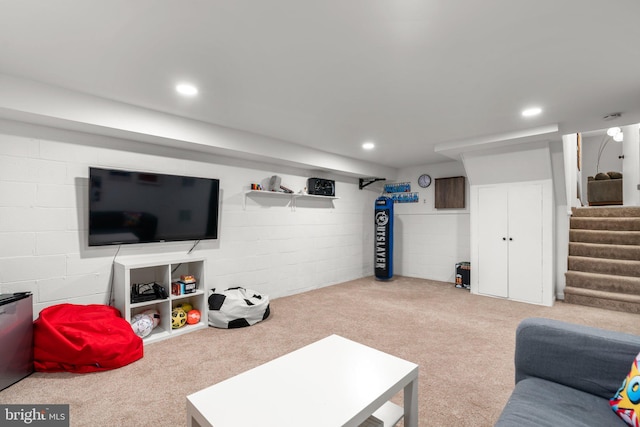 carpeted living room featuring concrete block wall, recessed lighting, and stairway