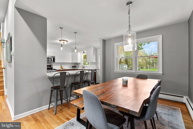 dining area featuring baseboards, a baseboard heating unit, and light wood-style floors