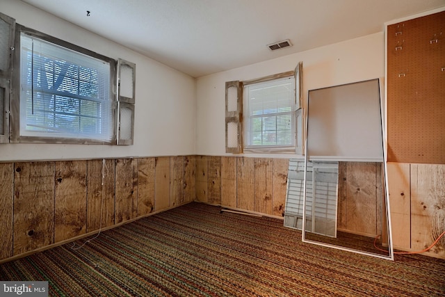 carpeted spare room featuring wainscoting, wood walls, and visible vents
