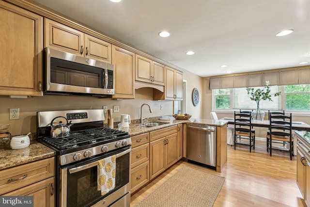 kitchen with a sink, stainless steel appliances, recessed lighting, light wood-style flooring, and light stone countertops