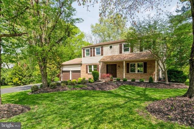 traditional-style home with a front yard, brick siding, an attached garage, and driveway