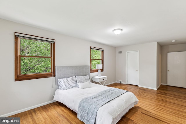 bedroom with baseboards, visible vents, and wood finished floors