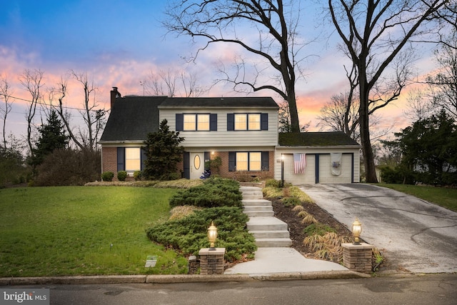 colonial-style house with a yard, brick siding, driveway, and a chimney