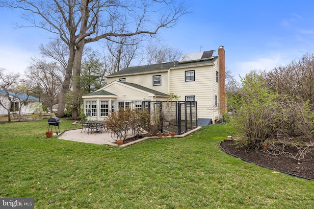 back of house with a patio, a chimney, solar panels, fence, and a lawn
