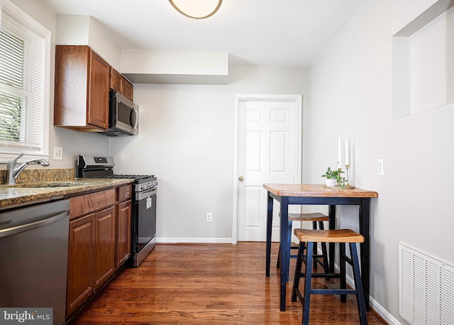 kitchen featuring dark wood-style flooring, visible vents, brown cabinetry, appliances with stainless steel finishes, and a sink