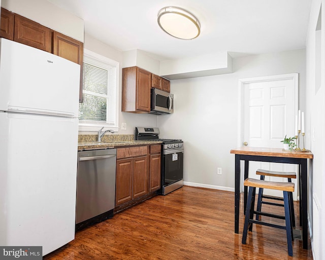 kitchen featuring baseboards, a sink, appliances with stainless steel finishes, dark wood-style floors, and light stone counters