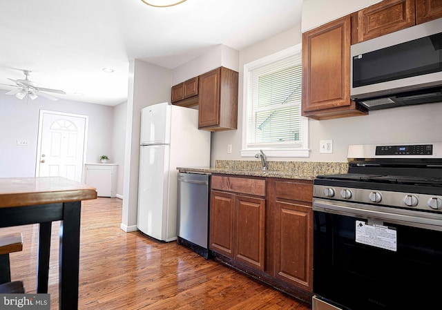 kitchen featuring baseboards, light stone counters, ceiling fan, stainless steel appliances, and wood finished floors